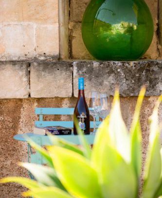 Una bottiglia di vino e due calici su un tavolino turchese nella corte, sotto una damigiana verde