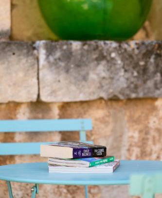 Libri impilati su un tavolino turchese addossato al muro in pietra della corte