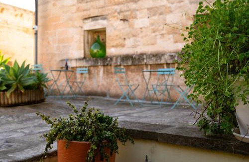 Tavolini e sedie turchesi allineati contro il muro in pietra della corte, con piante in vaso in primo piano